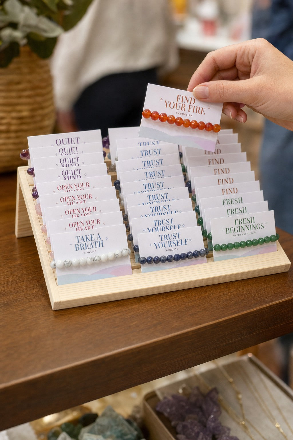 A customer lifts a carded carnelian bracelet out of the Intention Bracelet Display Kit on a shop counter.