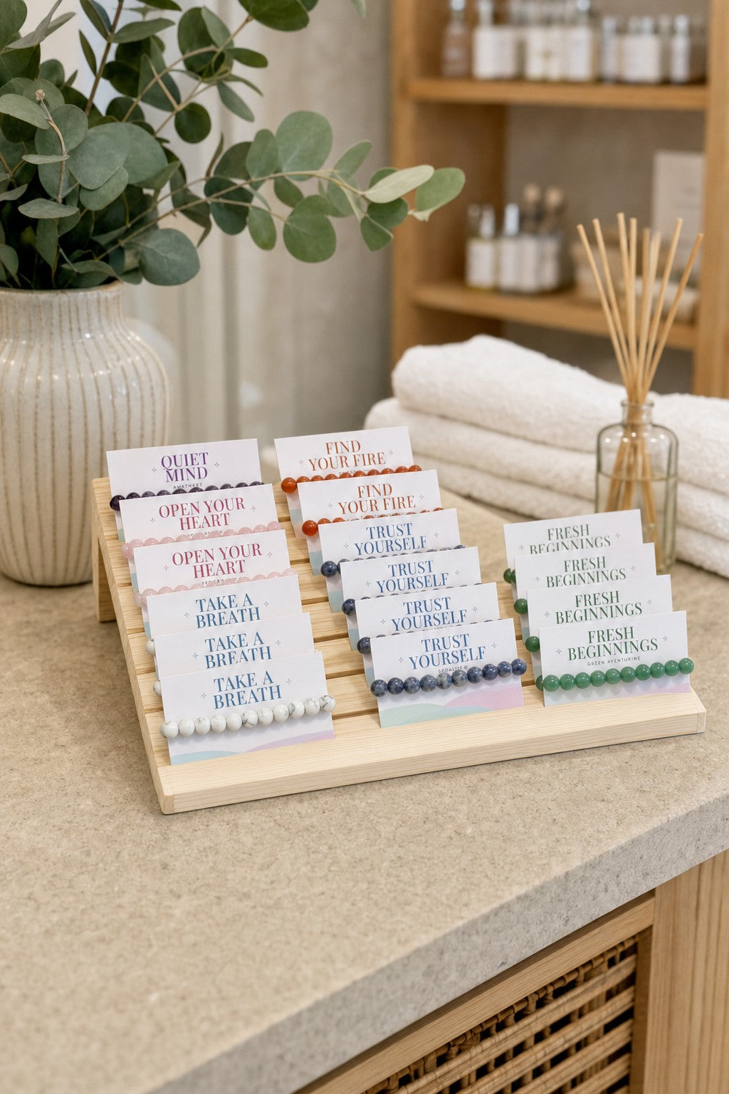 The Intention Bracelet Display Kit on a day spa's reception counter with eucalyptus and white towels.