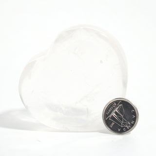 Clear Quartz Heart Bowl beside a Canadian dime for scale, showing the translucent quartz dish at about 2 inches across, on a clean white background. Stonebridge Imports.