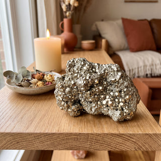 Pyrite Cluster Peru U#12 displayed on a wooden home altar shelf beside a lit candle, shown at true size in warm natural light.