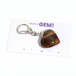One of the five golden-brown tiger eye heart charms from the pack, shown on its "you're a GEM!" gift backing card, hanging from its silver clasp on a clean white background. Stonebridge Imports.