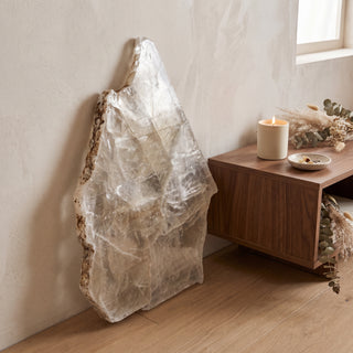Selenite Window Slab Unique #17 - 23" displayed leaning against a wall on a light oak floor beside a lit candle, shown at true size in warm natural light.
