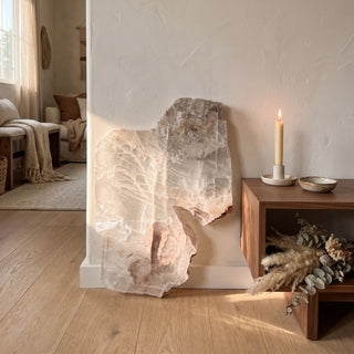 Selenite Window Slab Unique #18 - 21" displayed leaning against a wall on a light oak floor beside a lit candle, shown at true size in warm natural light.