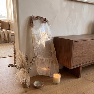 Selenite Window Slab Unique #20 - 26" displayed leaning against a wall on a light oak floor beside a lit candle, shown at true size in warm natural light.