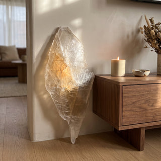 Selenite Window Slab Unique #21 - 32" displayed leaning against a wall on a light oak floor beside a lit candle, shown at true size in warm natural light.