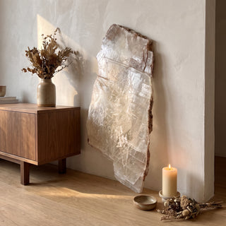 Selenite Window Slab Unique #22 - 30" displayed leaning against a wall on a light oak floor beside a lit candle, shown at true size in warm natural light.