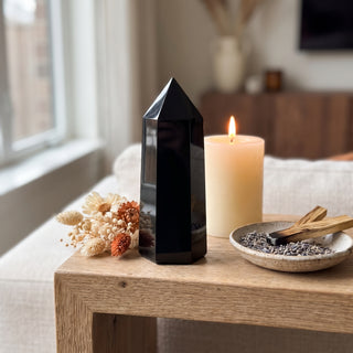 Black Obsidian Generator Unique #10 displayed on a wooden home altar shelf beside a lit candle and dried botanicals, shown at true size in warm natural light.