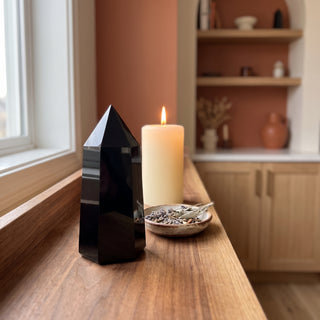 Black Obsidian Generator Unique #12 displayed on a wooden home altar shelf beside a lit candle and dried botanicals, shown at true size in warm natural light.
