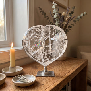 Clear Quartz Heart on Stand Unique #1 displayed on a wooden home altar shelf beside a candle, shown at true size in warm natural light.