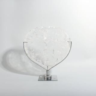 Clear Quartz Heart on Stand Unique #1, a polished clear quartz heart on a silver metal stand showing internal veils and rainbow inclusions, photographed on a clean white background. Stonebridge Imports.
