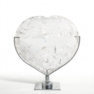 Clear Quartz Heart on Stand Unique #1, a polished clear quartz heart on a silver metal stand shown from an alternate angle on a clean white background. Stonebridge Imports.