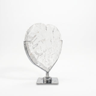 Clear Quartz Heart on Stand Unique #1, a polished clear quartz heart on a silver metal stand shown from an alternate angle on a clean white background. Stonebridge Imports.