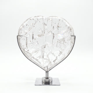 Clear Quartz Heart on Stand Unique #1, a polished clear quartz heart on a silver metal stand shown from an alternate angle on a clean white background. Stonebridge Imports.