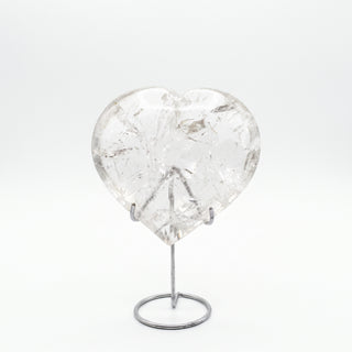 Clear Quartz Heart on Stand Unique #2, a polished clear quartz heart on a silver metal stand shown from an alternate angle on a clean white background. Stonebridge Imports.