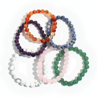 All six intention bracelets laid out together: amethyst, carnelian, sodalite, howlite, rose quartz and green aventurine 8mm beads, on white. Stonebridge Imports.