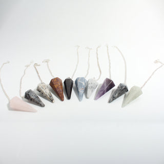 Mixed Stone Pendulums 10-Pack — ten faceted crystal point pendulums on silver chains in rose quartz, amethyst, howlite, angelite, moonstone, larvikite and green aventurine, on a clean white background. Stonebridge Imports.