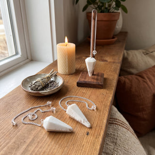 Scolecite Pendulum 6 Facet & Bead - 3 Pack on a wooden altar shelf beside a candle, three milky white scolecite pendulums at true size in warm natural light.