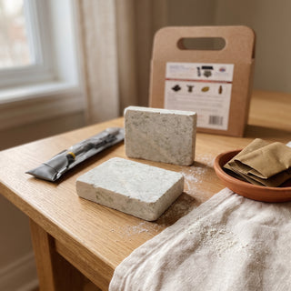 Soapstone Starter Carving Kit displayed on a warm oak craft table beside its rasp tool and folded sanding papers, shown at true size in soft natural light.