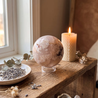 Flower Agate Sphere displayed on a wooden home altar shelf beside a candle, shown at true size in warm natural light.