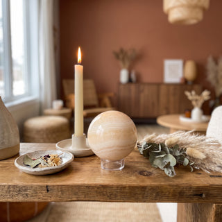 Orange Calcite Sphere - Mexico displayed on a wooden home altar shelf beside a candle, shown at true size in warm natural light.