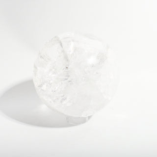 Clear Quartz Sphere Unique #18 - 6 1/4", a polished clear quartz sphere on a clear display stand shown from an alternate angle on a clean white background. Stonebridge Imports.