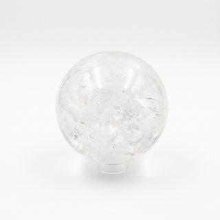 Clear Quartz Sphere Unique #19 - 6", a polished clear quartz sphere on a clear display stand showing internal veils and rainbow inclusions, photographed on a clean white background. Stonebridge Imports.