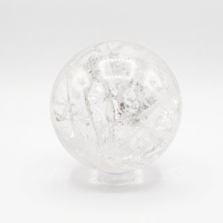 Clear Quartz Sphere Unique #19 - 6", a polished clear quartz sphere on a clear display stand shown from an alternate angle on a clean white background. Stonebridge Imports.
