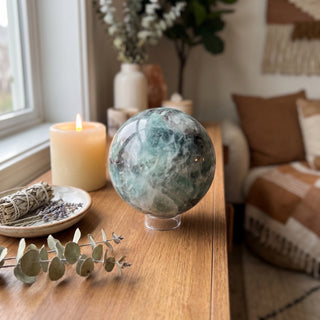 Fluorite Green and Purple Sphere Unique #11 displayed on a wooden home altar shelf beside a candle, shown at true size in warm natural light.