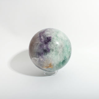 Fluorite Green and Purple Sphere Unique #12, showing green and purple fluorite with a golden-brown inclusion, photographed on a clean white background. Stonebridge Imports.