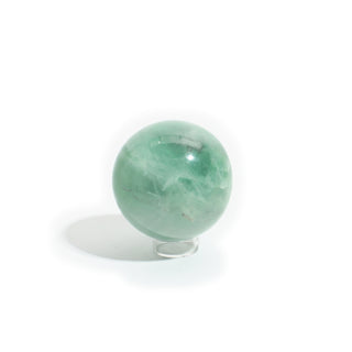 Fluorite Green and Purple Sphere Unique #16, a polished 3" translucent mint-green fluorite sphere with a pale white cloudy swirl through its centre, photographed on a clean white background. Stonebridge Imports.