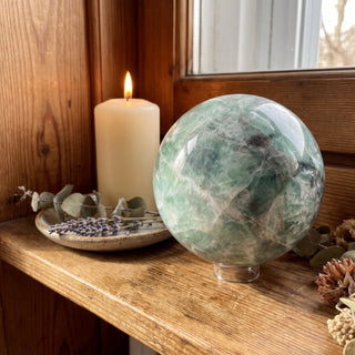 Fluorite Green and Purple Sphere Unique #9 displayed on a wooden home altar shelf beside a candle, shown at true size in warm natural light.