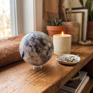 Black Tourmaline and Smoky Quartz Sphere Unique #1 displayed on a wooden home altar shelf beside a candle, shown at true size in warm natural light.