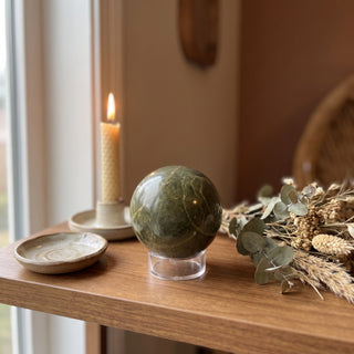 Vessonite Sphere displayed on a wooden home altar shelf beside a candle, resting on a clear display ring, shown at true size in warm natural light.