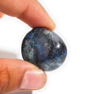 Large — Azurite Tumbled Stones, one dark navy stone with royal-blue azurite flecks held between thumb and finger for scale, photographed on a clean white background. Stonebridge Imports.