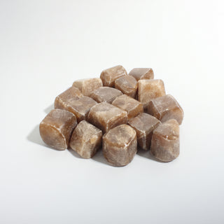 Medium — Honey Calcite Tumbled Stones - India, a pile of translucent honey-brown cube-shaped tumbled calcite, photographed on a clean white background. Stonebridge Imports.