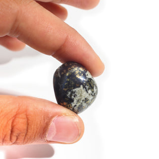 Large — Covellite Tumbled Stones, one black stone with gold pyrite and pale grey matrix held between thumb and finger for scale, photographed on a clean white background. Stonebridge Imports.