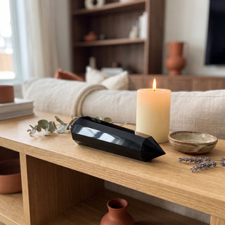 Black Obsidian Vogel Wand - 6" displayed on a wooden home altar shelf beside a lit candle and dried botanicals, shown at true size in warm natural light.