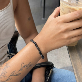 Black Agate bead bracelet worn on a tattooed forearm holding a coffee