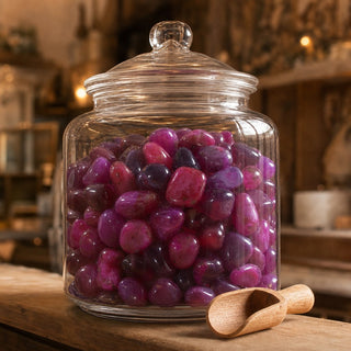 Agate Pink Tumbled Stones (Enhanced) in a glass apothecary jar with a scoop