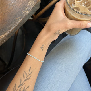Amazonite bead bracelet worn on a tattooed forearm holding a coffee