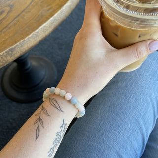 Aquamarine & Morganite bead bracelet worn on a tattooed forearm holding a coffee