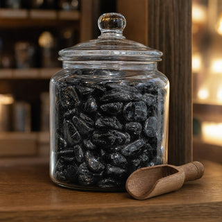 Black Tourmaline A Tumbled Stones in a glass apothecary jar with a scoop
