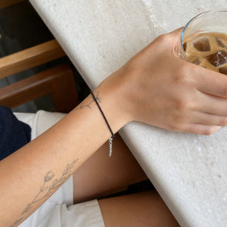 Black Tourmaline bead bracelet worn on a tattooed forearm holding a coffee