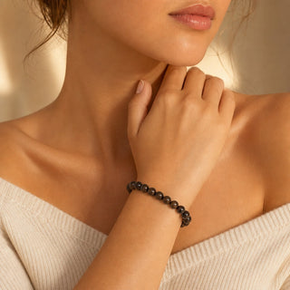 Bronzite bead bracelet worn with the fingertips resting at the collarbone