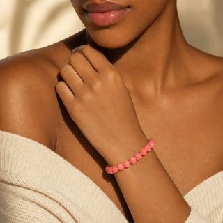 Pink Coral bead bracelet worn with the fingertips resting at the collarbone