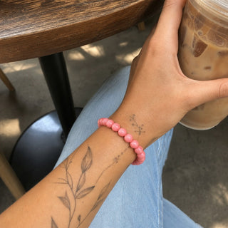 Pink Coral bead bracelet worn on a tattooed forearm holding a coffee