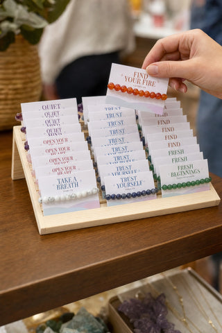 A customer lifts a carded carnelian bracelet out of the Intention Bracelet Display Kit on a shop counter.