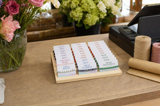 The Intention Bracelet Display Kit on a florist's counter beside the till, fresh flowers and kraft paper around it.
