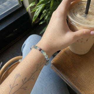 Fluorite bead bracelet worn on a tattooed forearm holding a coffee