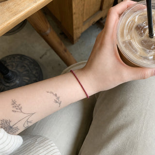 Garnet bead bracelet worn on a tattooed forearm holding a coffee